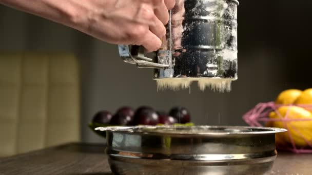 Close-up de uma mão feminina peneirando farinha com uma caneca peneira em uma tigela de metal na cozinha da casa. Cozinhar em casa Cozimento — Vídeo de Stock