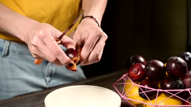 가정 부엌에서 여성의 손을 클로즈업하는 것은 매실 칼로 신선한 열매를 자르고 레몬 바구니 옆에 뼈를 꺼내고 있습니다. 건강한 음식과 비타민의 개념 — 비디오