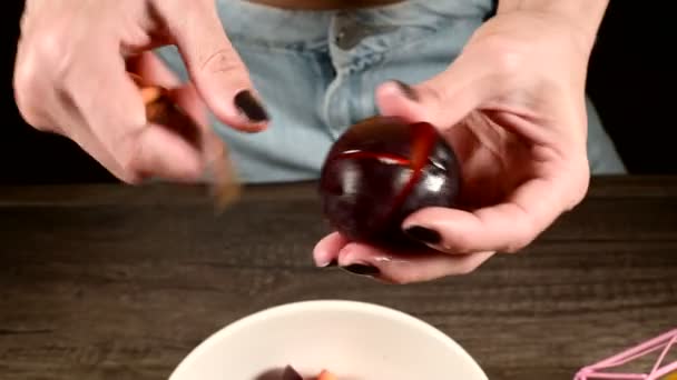 Primer plano de las manos femeninas en una cocina casera están cortando bayas frescas con un cuchillo de ciruela y tomando un hueso de ellos junto a una cesta de limones. El concepto de alimentos saludables y vitaminas — Vídeo de stock