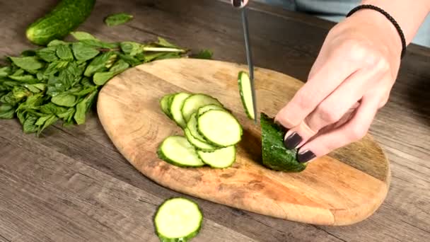 Крупный план женских рук, нарезающих огурцы на коляске на разделочной доске рядом с мятными листьями. Здоровая и здоровая вегетарианская еда — стоковое видео