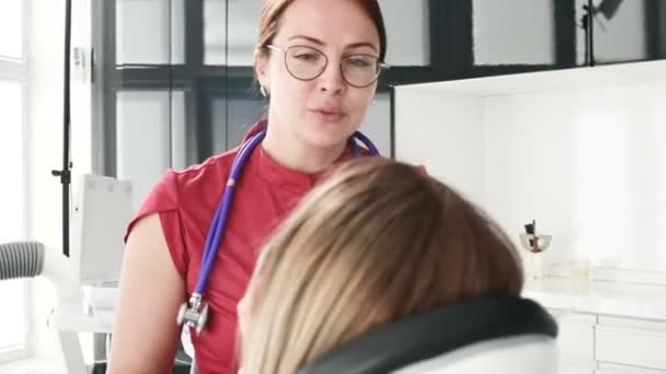 眼鏡をかけた歯科医の女性と相談する若い女の子が、駅のオフィスの椅子に座っている。医師と患者の会話 — ストック動画