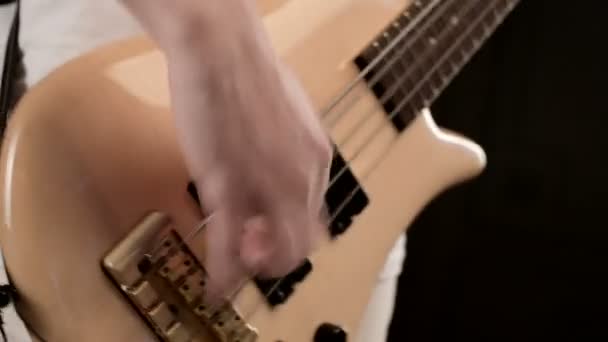 Jeune musicien en vêtements blancs avec une guitare basse beige sur fond noir. Guitare basse jeu de musique expressif — Video