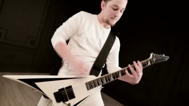 Стильный сольный гитарист с дредами на голове и в белой одежде на черном фоне, выразительно играющий на белой гитаре в черной студии — стоковое видео
