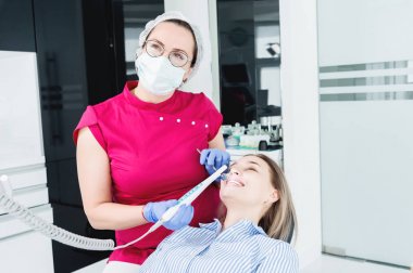 Gözlük ve tulum profesyonel bir diş hekimi kadın Led aydınlatma ile bir intraoral stamotolojik video kamera kullanarak diş sandalyesinde genç bir kızın ağız boşluğu inceler
