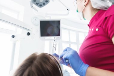 Gözlük ve tulum profesyonel bir diş hekimi kadın Led aydınlatma ile bir intraoral stamotolojik video kamera kullanarak diş sandalyesinde genç bir kızın ağız boşluğu inceler