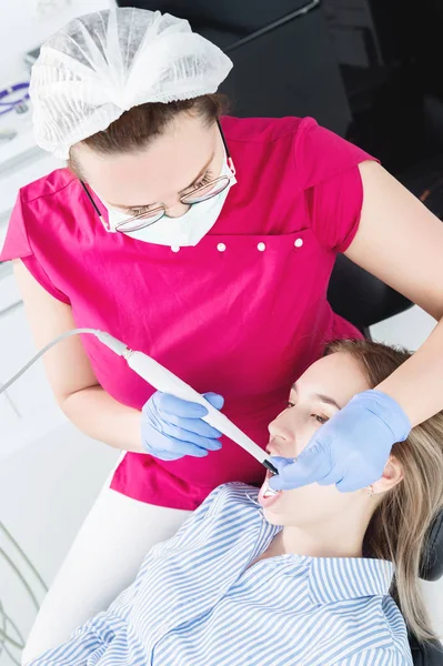 Close-up A professional dentist woman in glasses and overalls examines the oral cavity of a young girl in the dental chair using an intraoral stamotological video camera with LED illumination — Stock Photo, Image