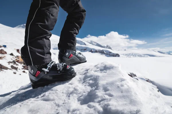 Zbliżenie się do nogi narciarzy w butach narciarskich bez nart stoi na Knoll błogości na tle gór w słoneczny dzień. Koncepcja skittura i Turystyka narciarska podróży — Zdjęcie stockowe