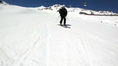 Siyah ekipman ve kayak direkleri ile beyaz kask yaşlı geniş açılı erkek kayakçı güneşli bir günde karlı bir yamaç üzerinde sürmek. Kış kayak sporları kavramı