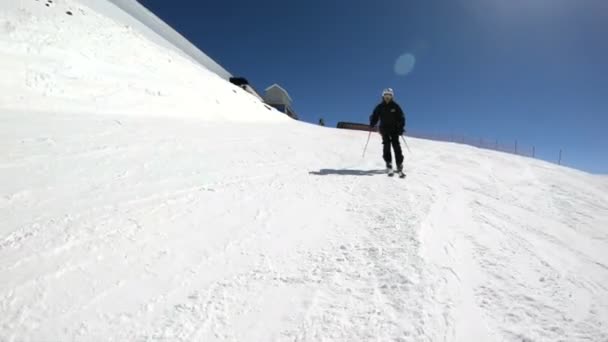 Siyah ekipman ve kayak direkleri ile beyaz kask yaşlı geniş açılı erkek kayakçı güneşli bir günde karlı bir yamaç üzerinde sürmek. Kış kayak sporları kavramı — Stok video