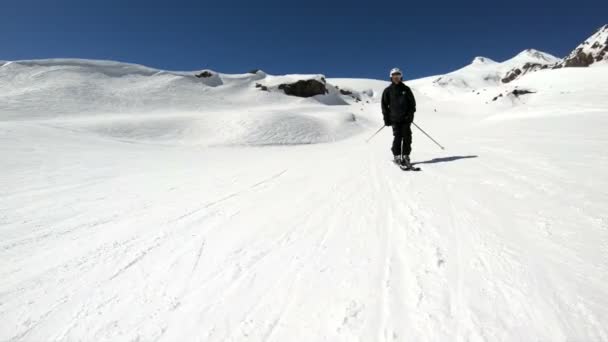 在阳光明媚的日子里，一名身着黑色装备、头戴白色头盔、带滑雪杆的广角男性滑雪者在雪坡上骑行。冬季滑雪运动的概念 — 图库视频影像