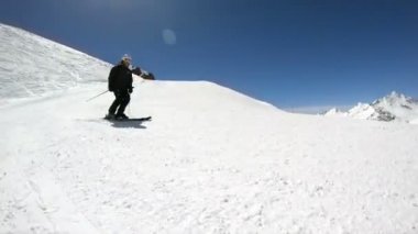 Siyah ekipman ve kayak direkleri ile beyaz kask yaşlı geniş açılı erkek kayakçı güneşli bir günde karlı bir yamaç üzerinde sürmek. Kış kayak sporları kavramı