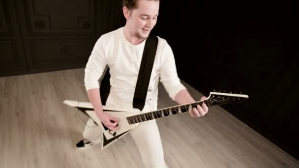 Stylish solo guitarist with dreadlocks on his head and in white clothes on a black background expressively playing the white guitar in a black studio — Stock Video