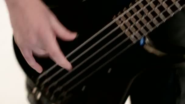 Νέος αρσενικός μουσικός με μαύρα ρούχα με μια μαύρη μπάσα κιθάρα σε λευκό φόντο. Μπάσο κιθαρίστα εκφραστικό παιχνίδι μουσικής — Αρχείο Βίντεο