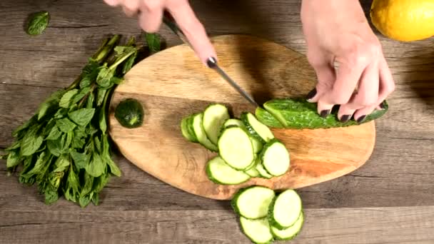 Primer plano de las manos femeninas rebanando pepinos en un cochecito en una tabla de cortar junto a las hojas de menta picadas. Comida Vegetariana Saludable y Saludable — Vídeo de stock