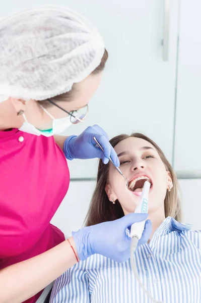 Nahaufnahme einer professionellen Zahnärztin in Brille und Overall untersucht die Mundhöhle eines jungen Mädchens im Zahnarztstuhl mit einer intraoralen stamotologischen Videokamera mit LED-Beleuchtung — Stockfoto