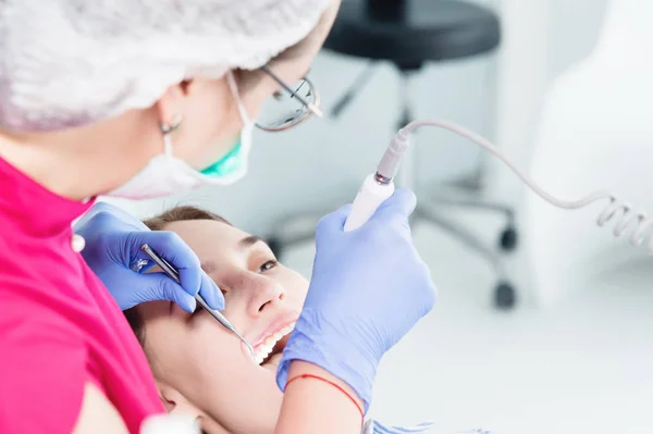 Κοντινό-up μια επαγγελματική γυναίκα οδοντίατρος σε γυαλιά και φόρμες εξετάζει την στοματική κοιλότητα ενός νεαρού κοριτσιού στην πολυθρόνα με χρήση ενδοστοματικής σταμολογικής βιντεοκάμερας με φωτισμό LED — Φωτογραφία Αρχείου