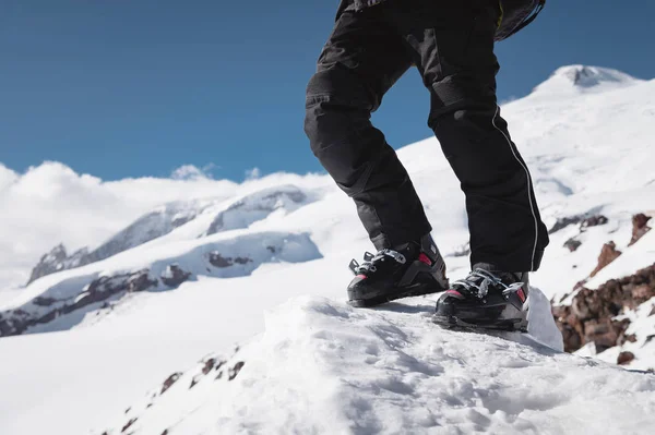Een close-up van een skiërs been in skischoenen zonder ski's staat op een Knoll van Bliss tegen de achtergrond van de bergen op een zonnige dag. Het concept van skittura en wandelen ski Travel — Stockfoto