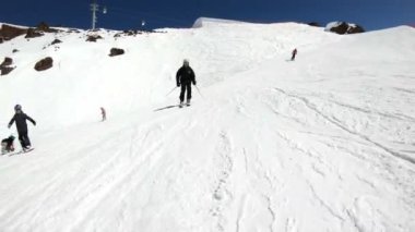 Siyah ekipman ve kayak direkleri ile beyaz kask yaşlı geniş açılı erkek kayakçı güneşli bir günde karlı bir yamaç üzerinde sürmek. Kış kayak sporları kavramı