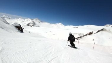 Siyah ekipman ve kayak direkleri ile beyaz kask yaşlı geniş açılı erkek kayakçı güneşli bir günde karlı bir yamaç üzerinde sürmek. Kış kayak sporları kavramı
