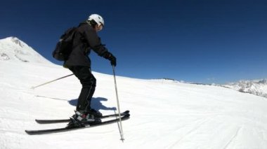 Siyah ekipman ve kayak direkleri ile beyaz kask yaşlı geniş açılı erkek kayakçı güneşli bir günde karlı bir yamaç üzerinde sürmek. Kış kayak sporları kavramı