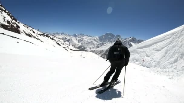 在阳光明媚的日子里，一名身着黑色装备、头戴白色头盔、带滑雪杆的广角男性滑雪者在雪坡上骑行。冬季滑雪运动的概念 — 图库视频影像