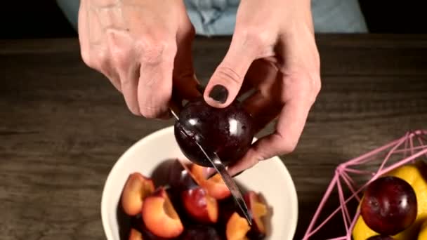 Close-up de mãos femininas em uma cozinha doméstica estão cortando bagas frescas com uma faca de ameixa e tirando um osso deles ao lado de um cesto de limões. O conceito de alimentos saudáveis e vitaminas — Vídeo de Stock