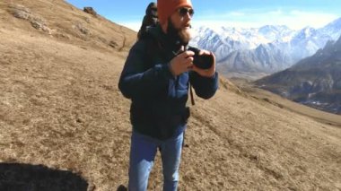 Güneş gözlüğü ve elinde bir refleks kamera ile bir şapka mutlu sakallı gezgin fotoğrafçı portresi ve dağların arka plan karşı fotoğraf çekmek. Fotoğraf seyahat konsepti