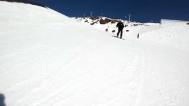 Siyah ekipman ve kayak direkleri ile beyaz kask yaşlı geniş açılı erkek kayakçı güneşli bir günde karlı bir yamaç üzerinde sürmek. Kış kayak sporları kavramı