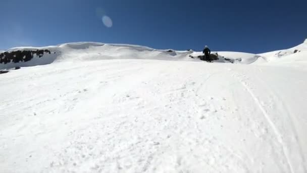 Een groothoek mannelijke skiër gerijpt in zwarte uitrusting en witte helm met skistokken rijdt op een besneeuwde helling op een zonnige dag. Het concept van winter skisporten — Stockvideo