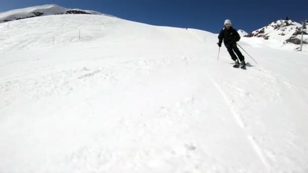 A nagy látószögű férfi síelő éves fekete berendezések és fehér sisak sí pólusok lovagol egy havas lejtőn egy napsütéses napon. A téli Sísportok koncepciója — Stock videók