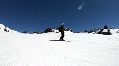 Siyah ekipman ve kayak direkleri ile beyaz kask yaşlı geniş açılı erkek kayakçı güneşli bir günde karlı bir yamaç üzerinde sürmek. Kış kayak sporları kavramı