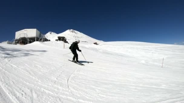 Un esquiador masculino de gran angular envejecido en equipo negro y casco blanco con bastones de esquí paseos en una ladera nevada en un día soleado. El concepto de esquí de invierno — Vídeos de Stock
