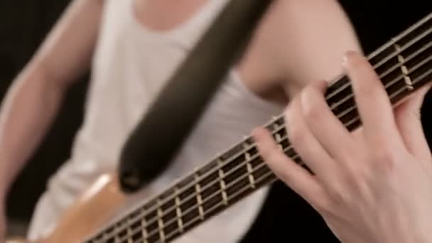 Młody męski muzyk w białych ubraniach z beżową gitarą basową na czarnym tle. Gitara basowa odtwarzacz ekspresyjny gra muzyczna — Wideo stockowe