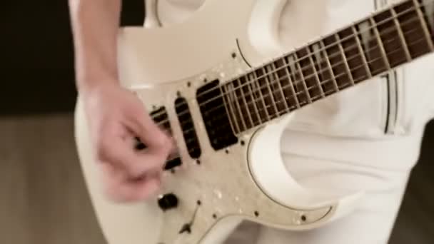 Close-up Elegante guitarrista rítmico con diferentes ojos en ropa blanca sobre un fondo negro tocando expresivamente la guitarra blanca en un estudio negro — Vídeos de Stock