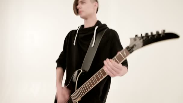 Elegante guitarrista rítmico con diferentes ojos en ropa negra sobre un fondo blanco tocando expresivamente la guitarra negra en un estudio blanco — Vídeo de stock