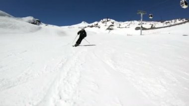 Siyah ekipman ve kayak direkleri ile beyaz kask yaşlı geniş açılı erkek kayakçı güneşli bir günde karlı bir yamaç üzerinde sürmek. Kış kayak sporları kavramı