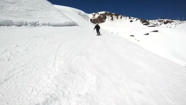 晴れた日には、黒い装備と白いヘルメットを持つ広角の男性スキーヤーが雪の斜面に乗ります。ウィンタースキースポーツのコンセプト — ストック動画