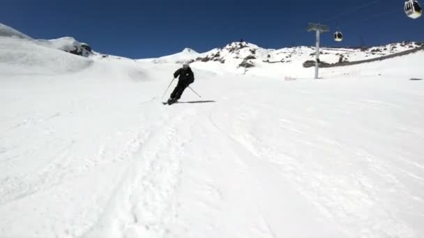 Ein Weitwinkelskiläufer in schwarzer Ausrüstung und weißem Helm mit Skistöcken fährt an einem sonnigen Tag auf einem schneebedeckten Hang. das Konzept des Wintersports — Stockvideo