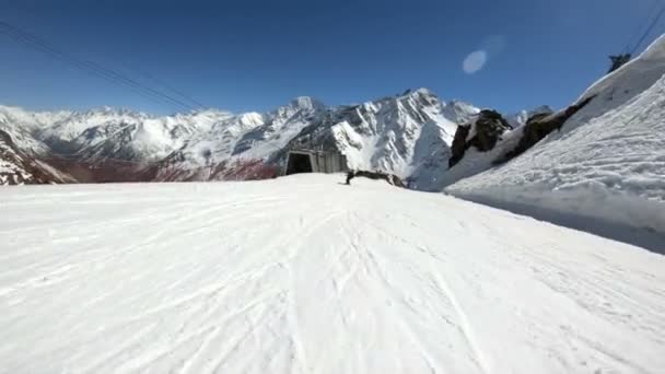 Een groothoek mannelijke skiër gerijpt in zwarte uitrusting en witte helm met skistokken rijdt op een besneeuwde helling op een zonnige dag. Het concept van winter skisporten — Stockvideo