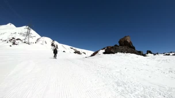 Μια ευρεία γωνία αρσενικό σκιέρ ηλικίας με μαύρο εξοπλισμό και λευκό κράνος με μπαστούνια του σκι βόλτες σε μια χιονισμένη πλαγιά σε μια ηλιόλουστη μέρα. Η έννοια των χειμερινών σπορ σκι — Αρχείο Βίντεο