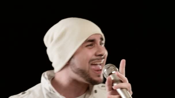 Close-up frontman wokalista pop rock ze stylową brodą w białych ubrań i kapelusz z mikrofonem w dłoniach ekspresyjnie agresywnie śpiewa w studiu na tle czarnych ścian — Wideo stockowe