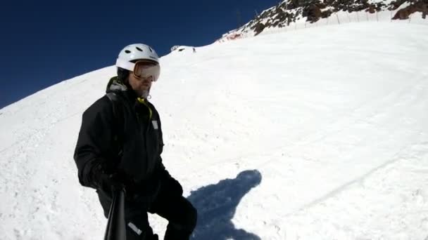 Un selfie grandangolare maschile invecchiato in attrezzatura nera e casco bianco cavalca su un pendio innevato in una giornata di sole. Il concetto di sport sciistici invernali — Video Stock