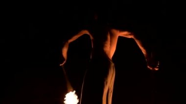 Düşük anahtar. Uzun saçlı ve çıplak gövde ile genç erkek siyah bir gece video yavaş hareket açık havada yanan meşale döner. Modern fakir bir yanan personel ile hileler yapar