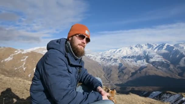Güneş gözlüğü ve şapkalı sakallı bir gezginin portresi dağların arka planında bir kayanın üzerinde yer alır. hayır diyor — Stok video