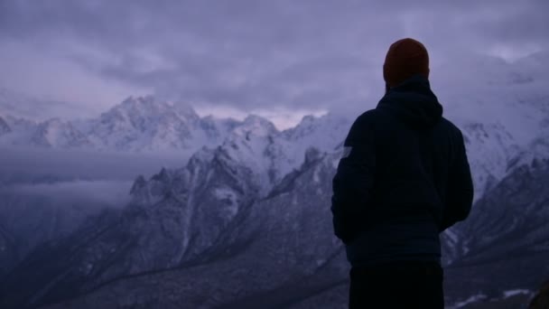 Portrét mladého vousatého mužského cestovatele za soumraku v horách. Zůstaňte vážně přemýšlet a Rozhlédni se. Teple oblečený chlapík na pozadí zasněžených hor — Stock video