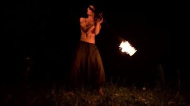 Düşük anahtar. Uzun saçlı ve çıplak gövde ile genç erkek siyah bir gece video yavaş hareket açık havada yanan meşale döner. Modern fakir bir yanan personel ile hileler yapar