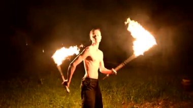 Düşük anahtar. Uzun saçlı ve çıplak gövde ile genç erkek siyah bir gece video yavaş hareket açık havada yanan meşale döner. Modern fakir bir yanan personel ile hileler yapar