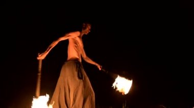 Düşük anahtar. Uzun saçlı ve çıplak gövde ile genç erkek siyah bir gece video yavaş hareket açık havada yanan meşale döner. Modern fakir bir yanan personel ile hileler yapar