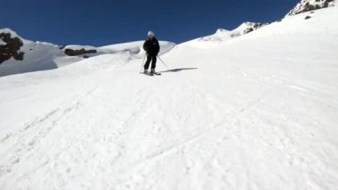Siyah ekipman ve kayak direkleri ile beyaz kask yaşlı geniş açılı erkek kayakçı güneşli bir günde karlı bir yamaç üzerinde sürmek. Kış kayak sporları kavramı