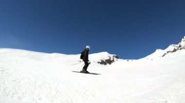 Siyah ekipman ve kayak direkleri ile beyaz kask yaşlı geniş açılı erkek kayakçı güneşli bir günde karlı bir yamaç üzerinde sürmek. Kış kayak sporları kavramı